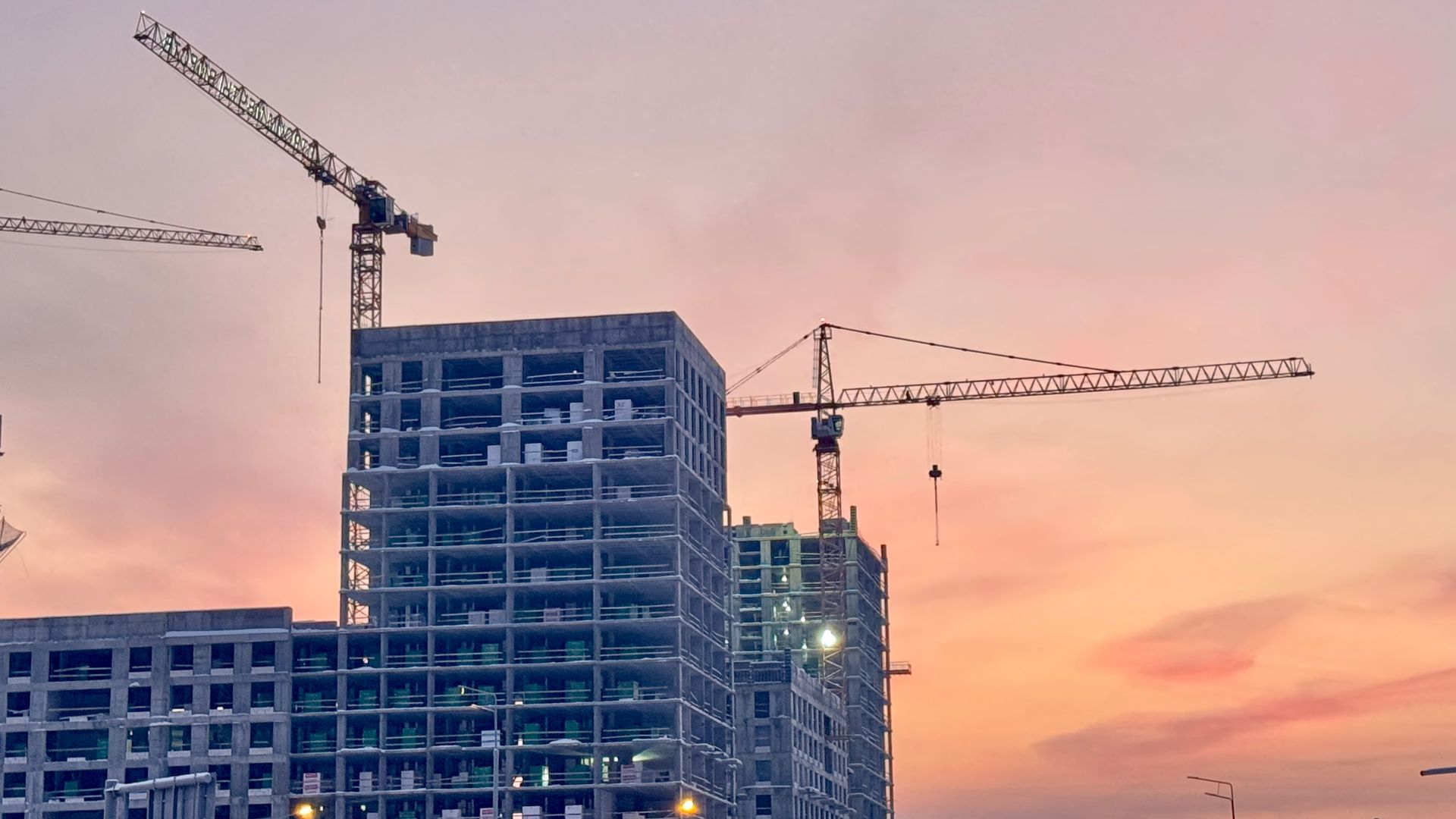 Construction site with high-rise buildings and cranes against a pink sunset sky