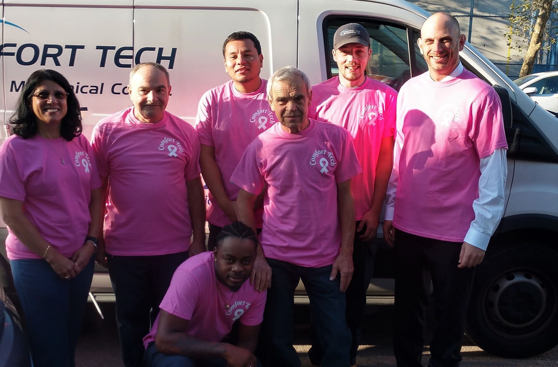 Six people in pink shirts posing in front of a medical van and sign.