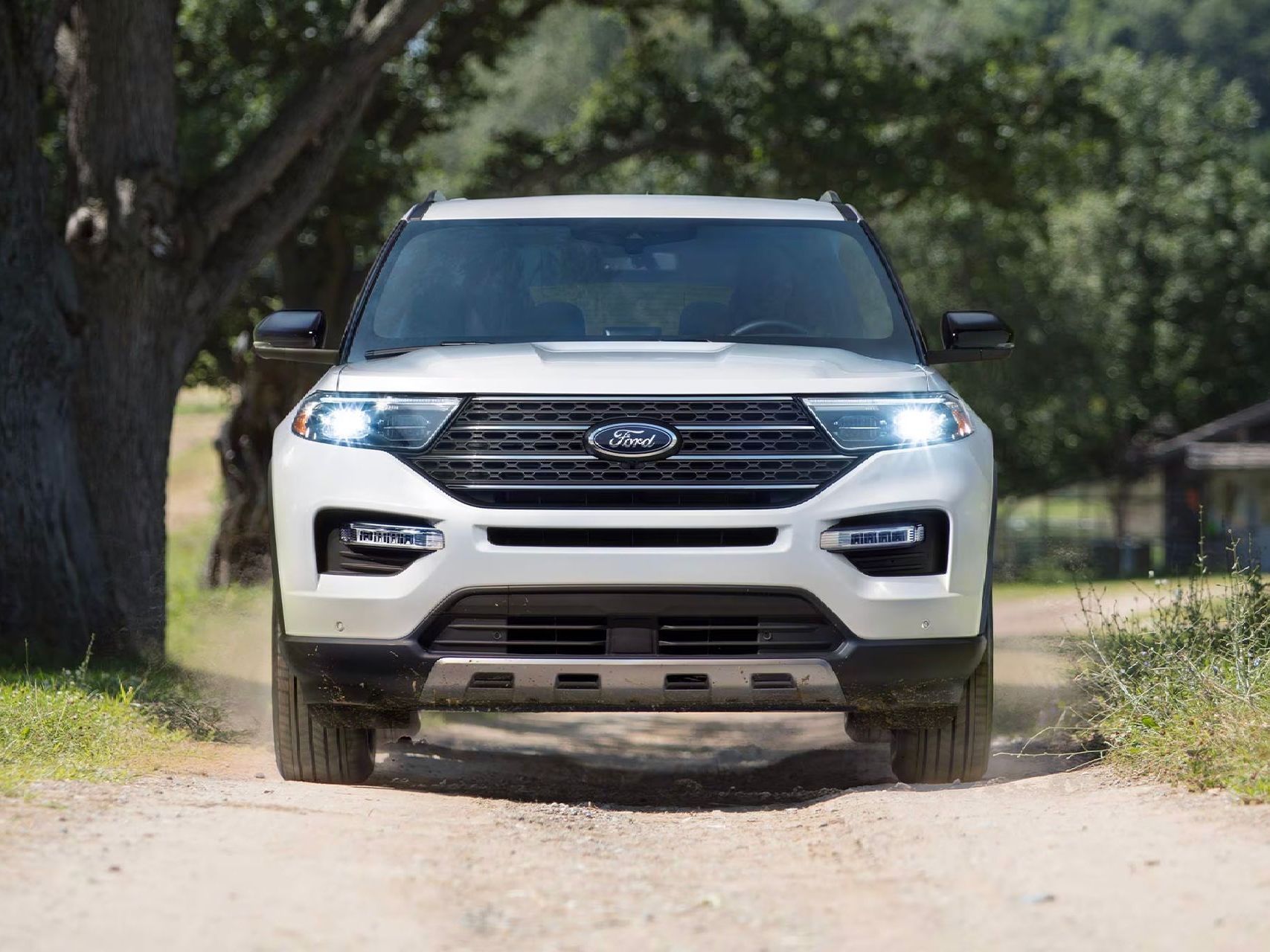A white ford explorer is driving down a dirt road.
