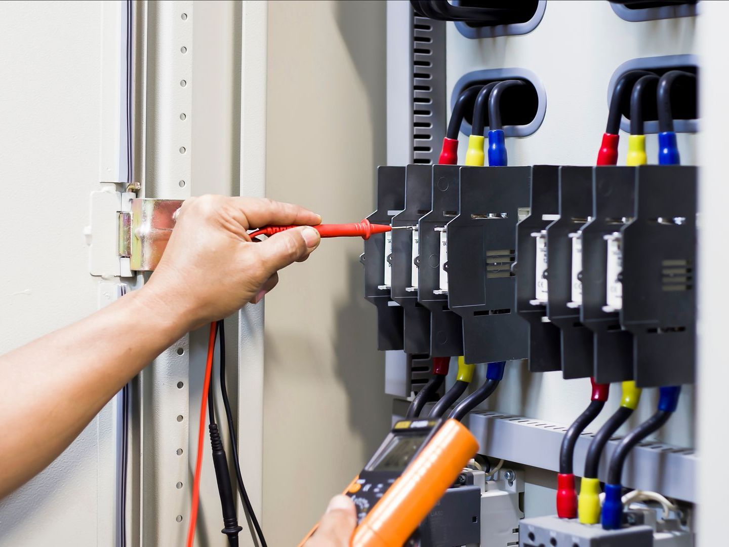 A person is working on an electrical box with a multimeter.