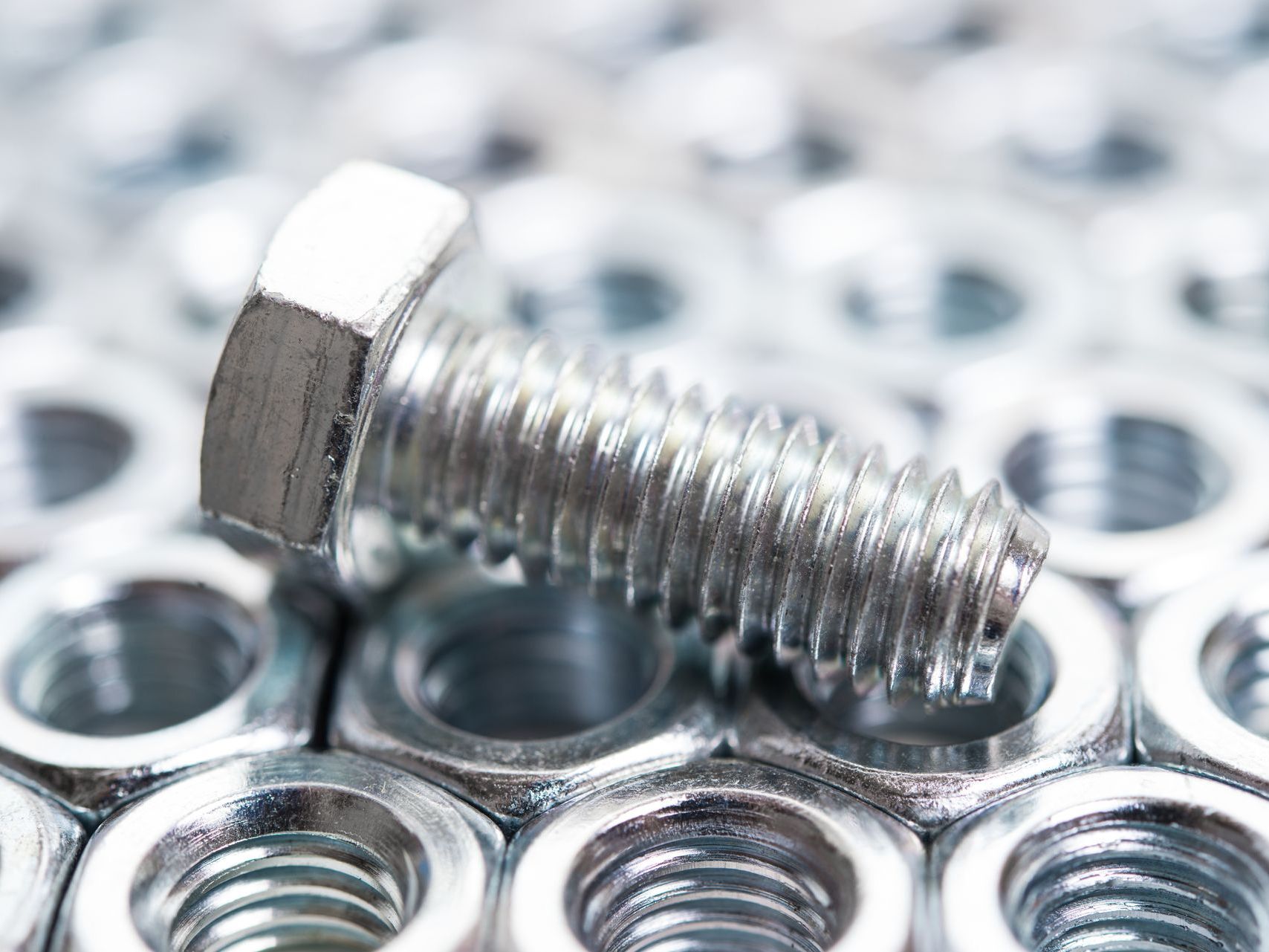 A screw is sitting on top of a pile of nuts.