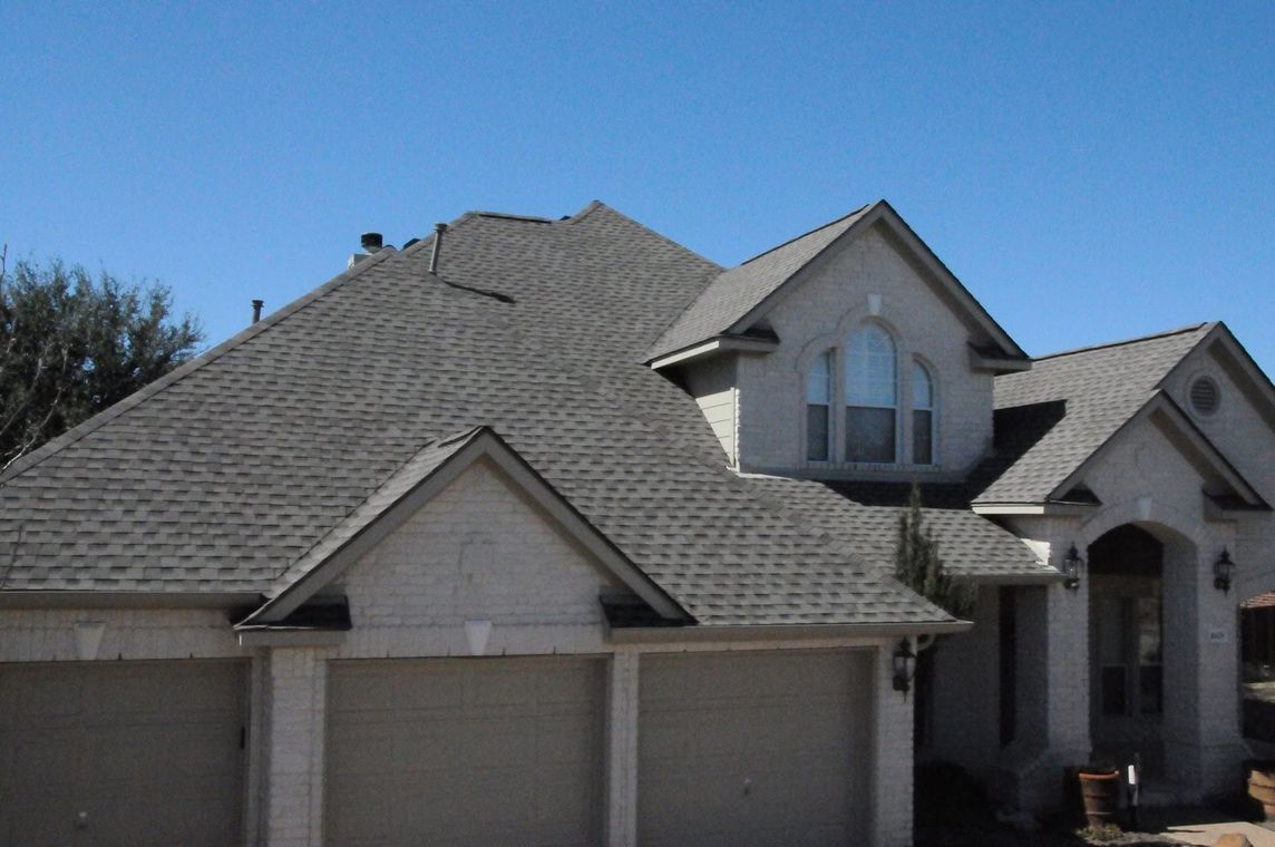 Suburban house with gray shingle roof and beige garage doors under a blue sky