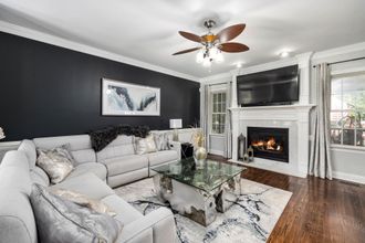 Bright living room with white sectional sofa, fireplace, wall TV, glass coffee table, and dark accent wall