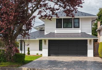 Two-story suburban house with white siding, dark garage door, and a tree in front