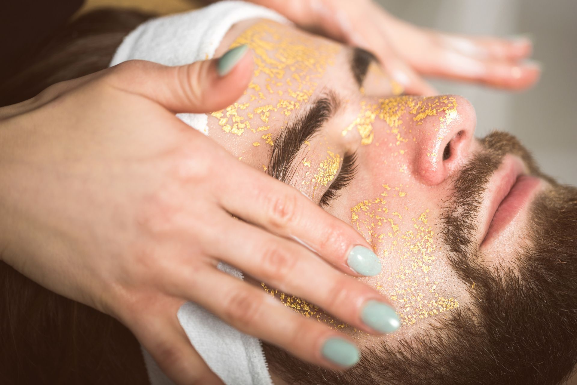 Person receiving a gold facial mask while lying back with eyes closed