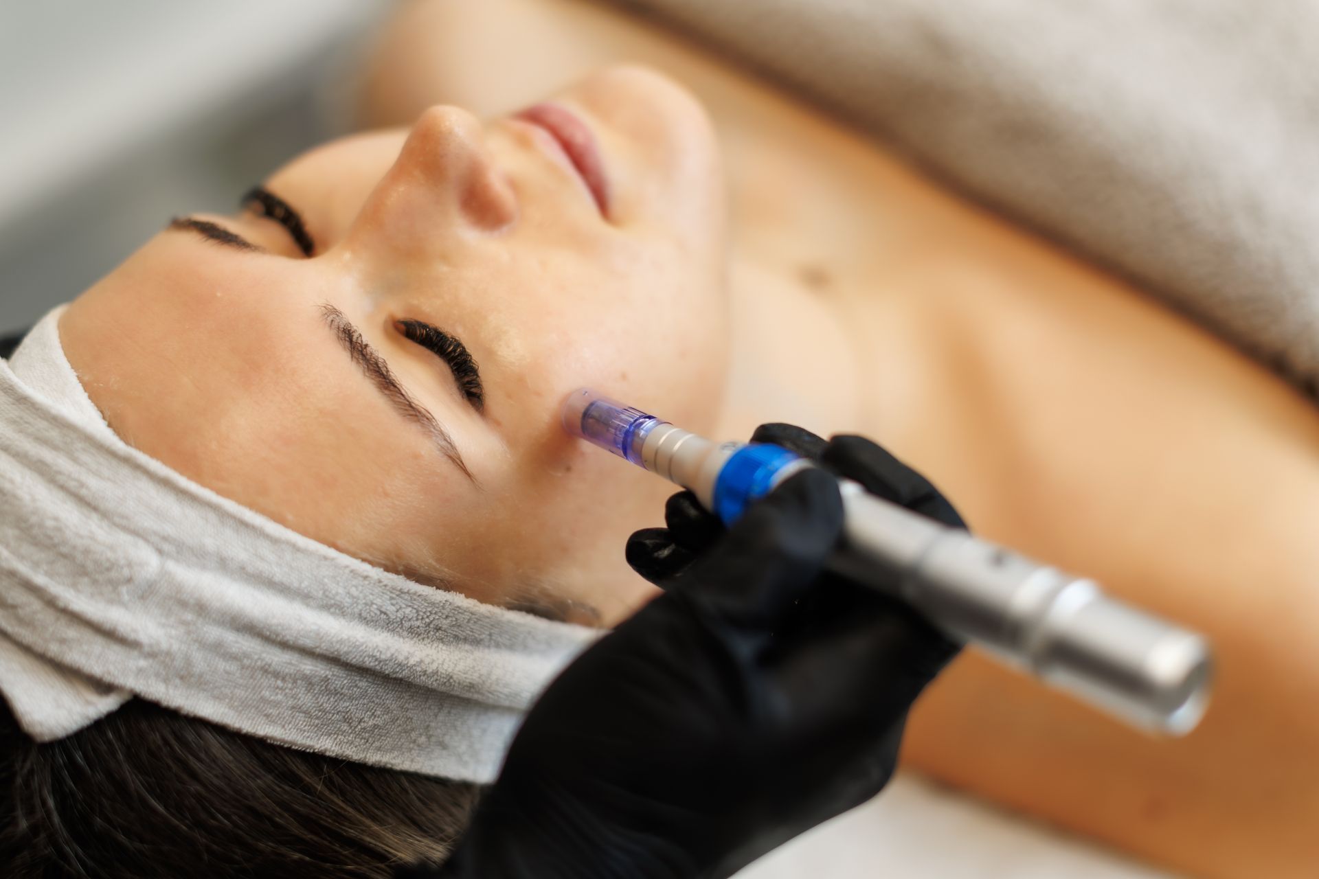 Facial treatment with a gloved hand applying a cosmetic device near the cheek and temple