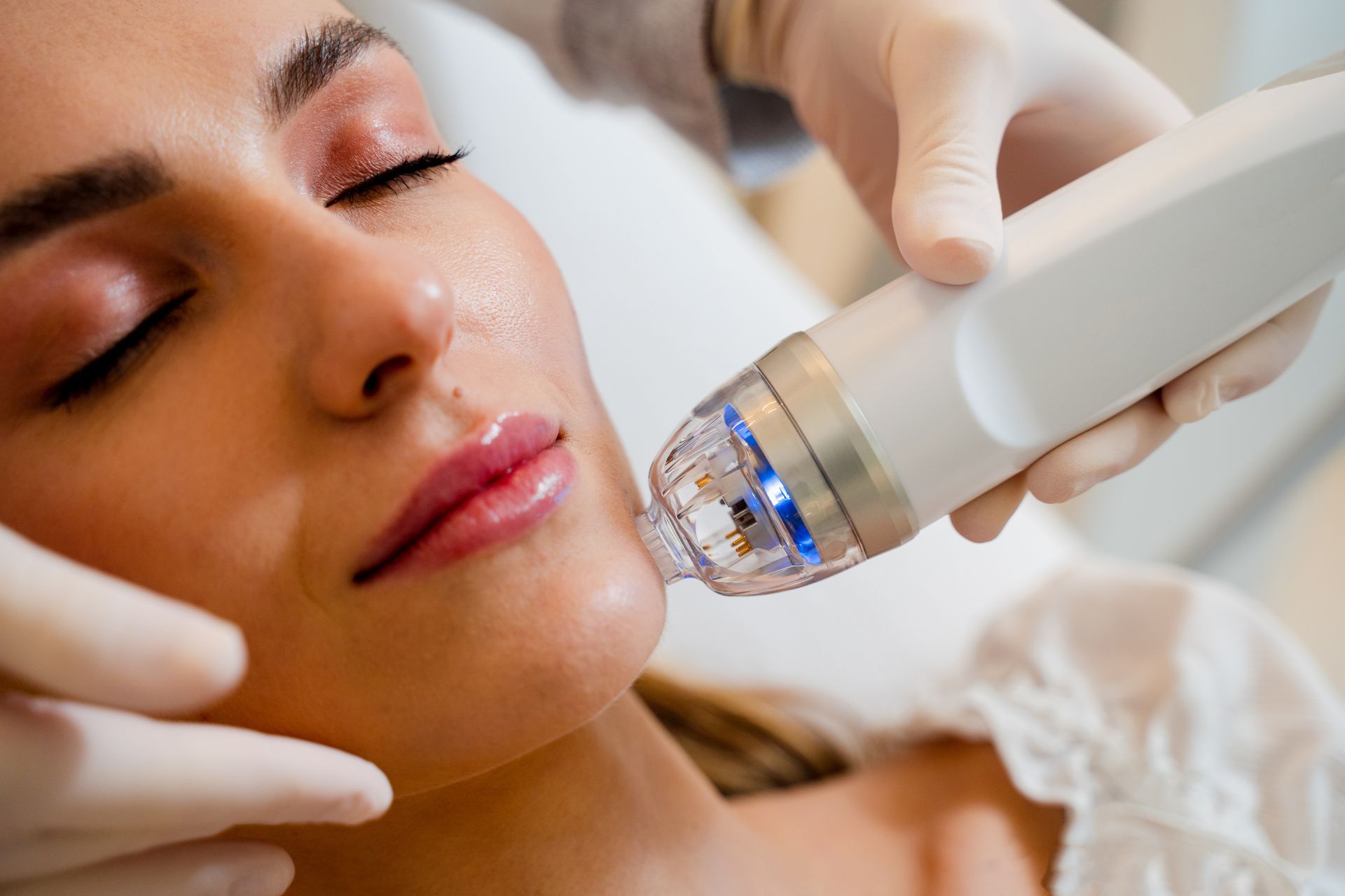 A woman receiving a facial treatment with a handheld skincare device while lying on a bed