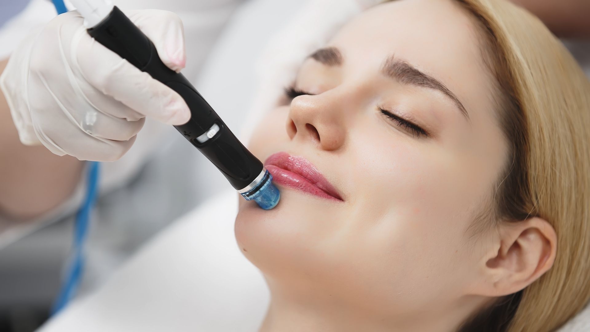 A spa facial treatment with a gloved hand using a blue-tipped device on a woman's lips