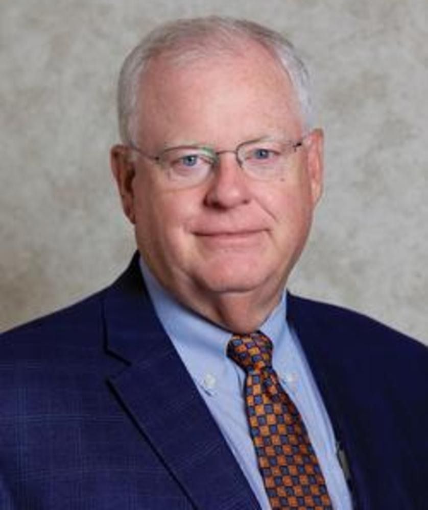 Portrait of a man in a blue suit and patterned tie against a neutral studio backdrop