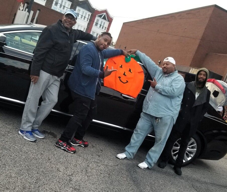 A group of men standing in front of a car holding an orange pumpkin