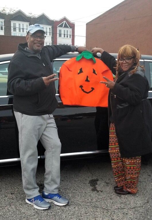 A man and woman holding an orange pumpkin with a face on it