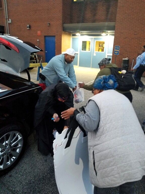 A group of people are standing around a car with the trunk open
