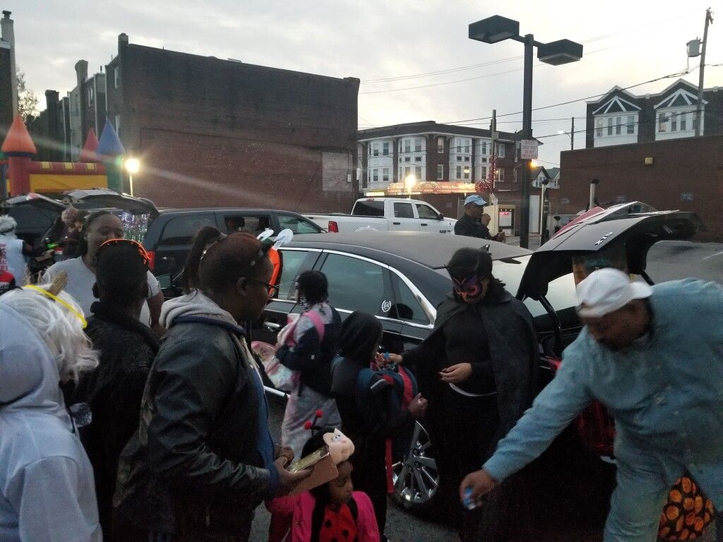 A group of people are standing around a car in a parking lot.