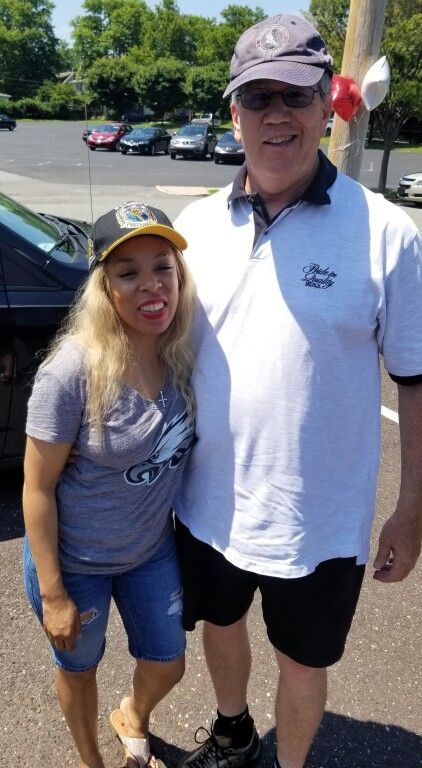 A man and a woman are posing for a picture in a parking lot.