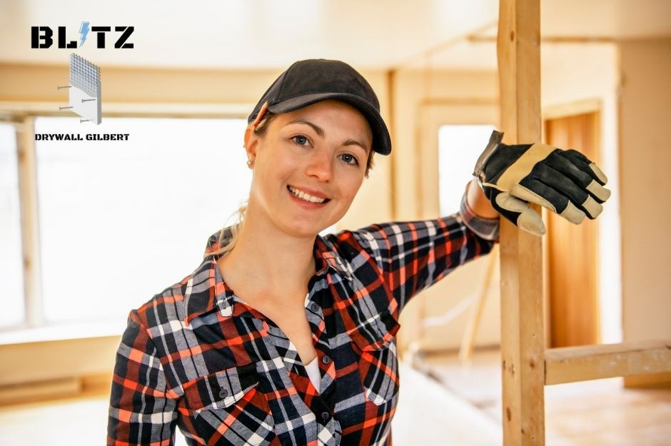 A drywall repair company worker in plaid shirt and cap holds a putty knife in wooden frame in a residential construction site near E Eagle Rock Dr, and N Boulder Dr, Fountain Hills, AZ.