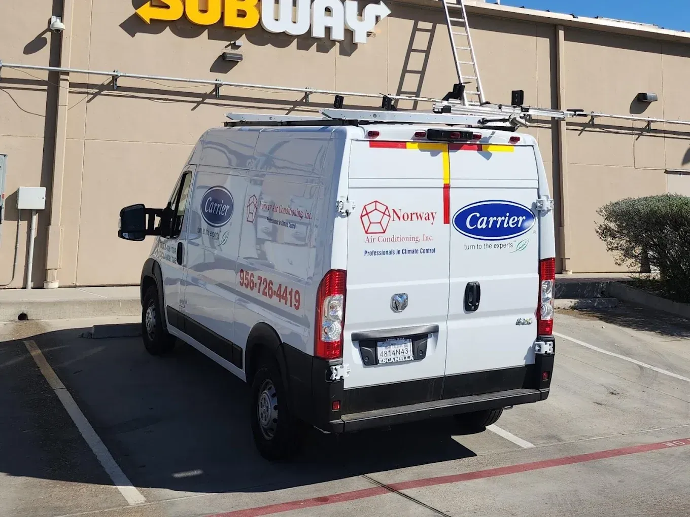 White service van parked in front of a Subway sign. A ladder rests on the building.