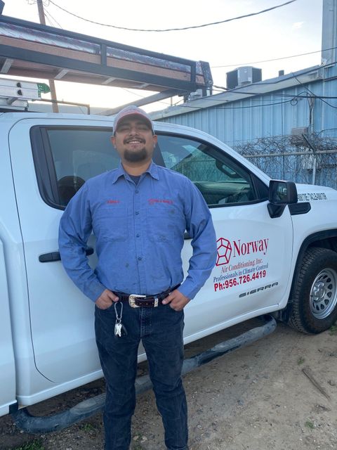 Man in blue shirt stands by white work truck with company logo.