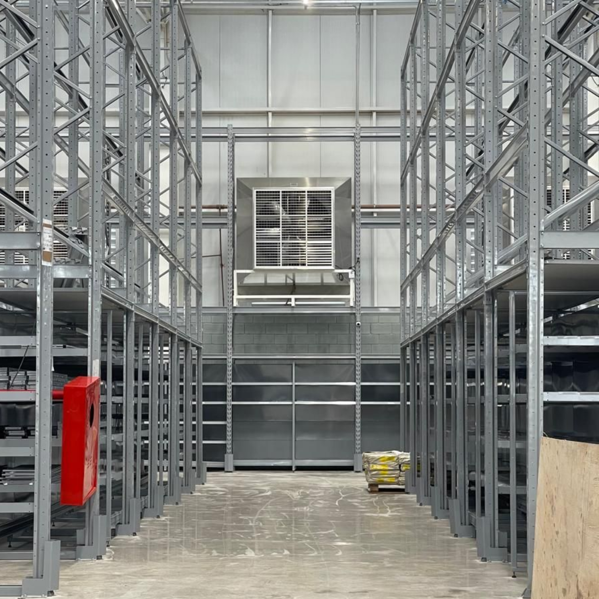 Consumidores percorrem os corredores de uma loja de armazém com grandes ventiladores industriais instalados acima das prateleiras de mercadorias embaladas.