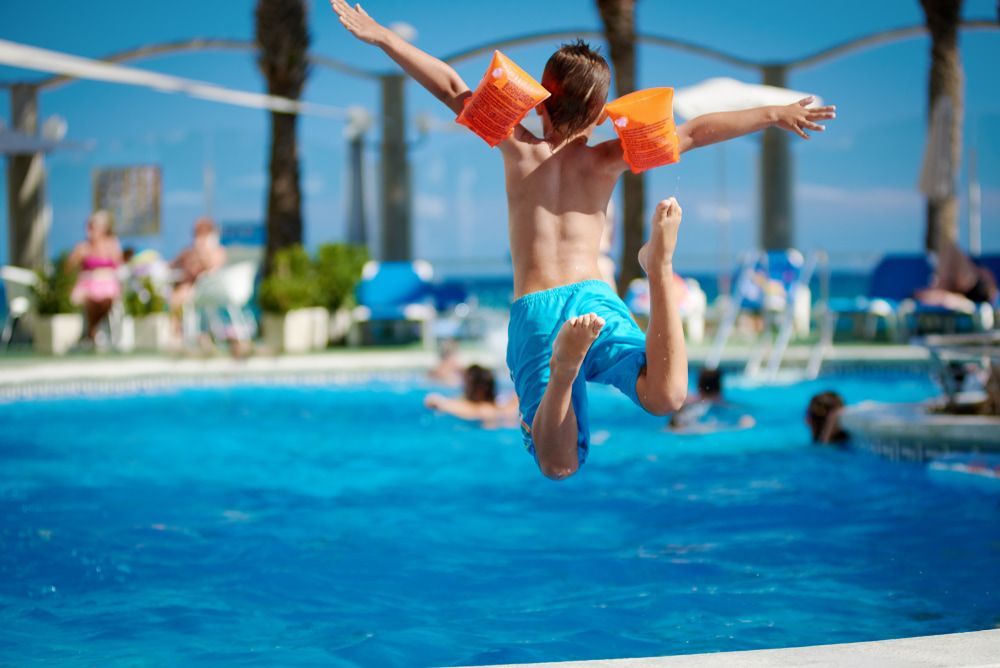 A Young Boy Is Jumping Into A Swimming Pool — Holiday Coast Pools & Water In Woolgoolga, NSW