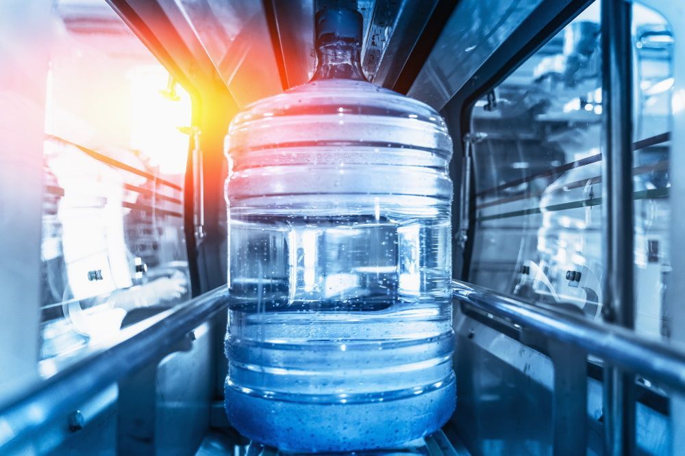 A Large Bottle Of Water Is On A Conveyor Belt In A Factory — Holiday Coast Pools & Water In Coffs Harbour, NSW