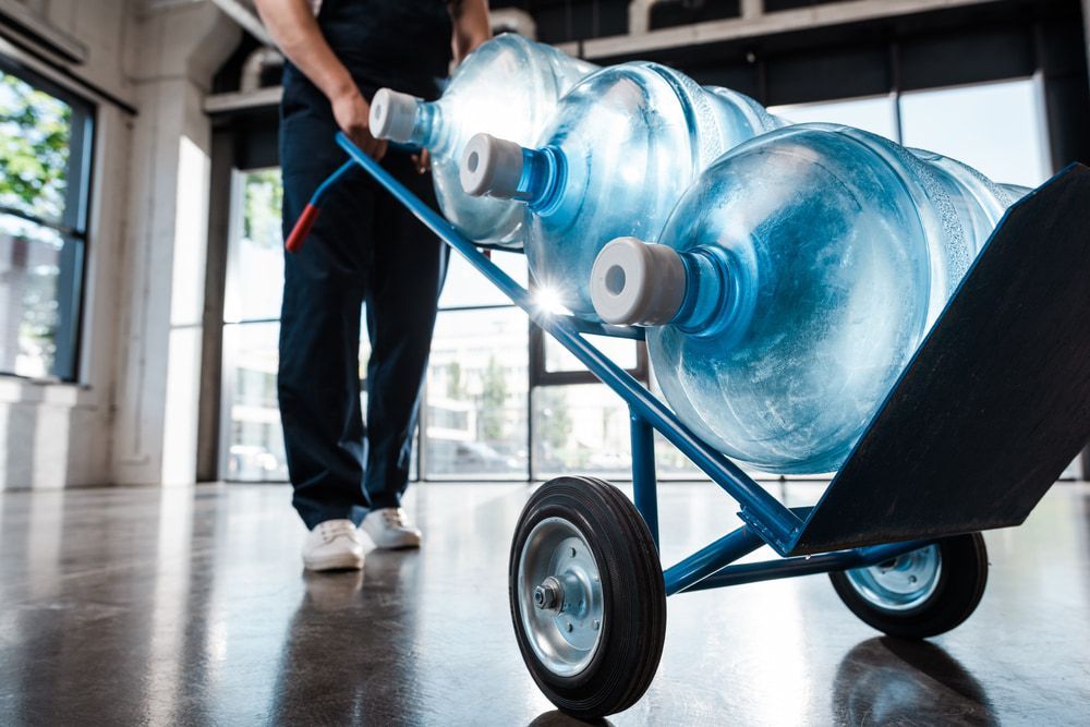 A Man Is Pushing A Cart Filled With Water Bottles — Holiday Coast Pools & Water In Coffs Harbour, NSW