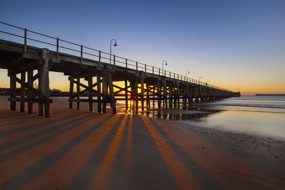 A Pier Leading Into The Ocean At Sunset — Holiday Coast Pools & Water In Coffs Harbour, NSW