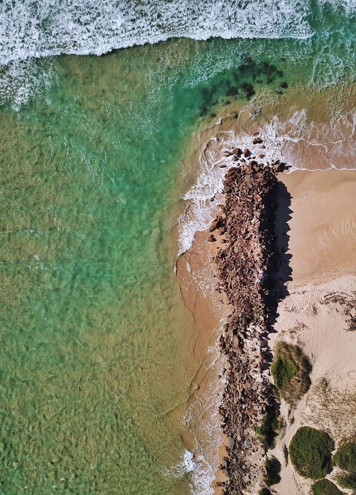 An Aerial View Of A Beach With Waves Crashing On The Shore — Holiday Coast Pools & Water In Urunga, NSW