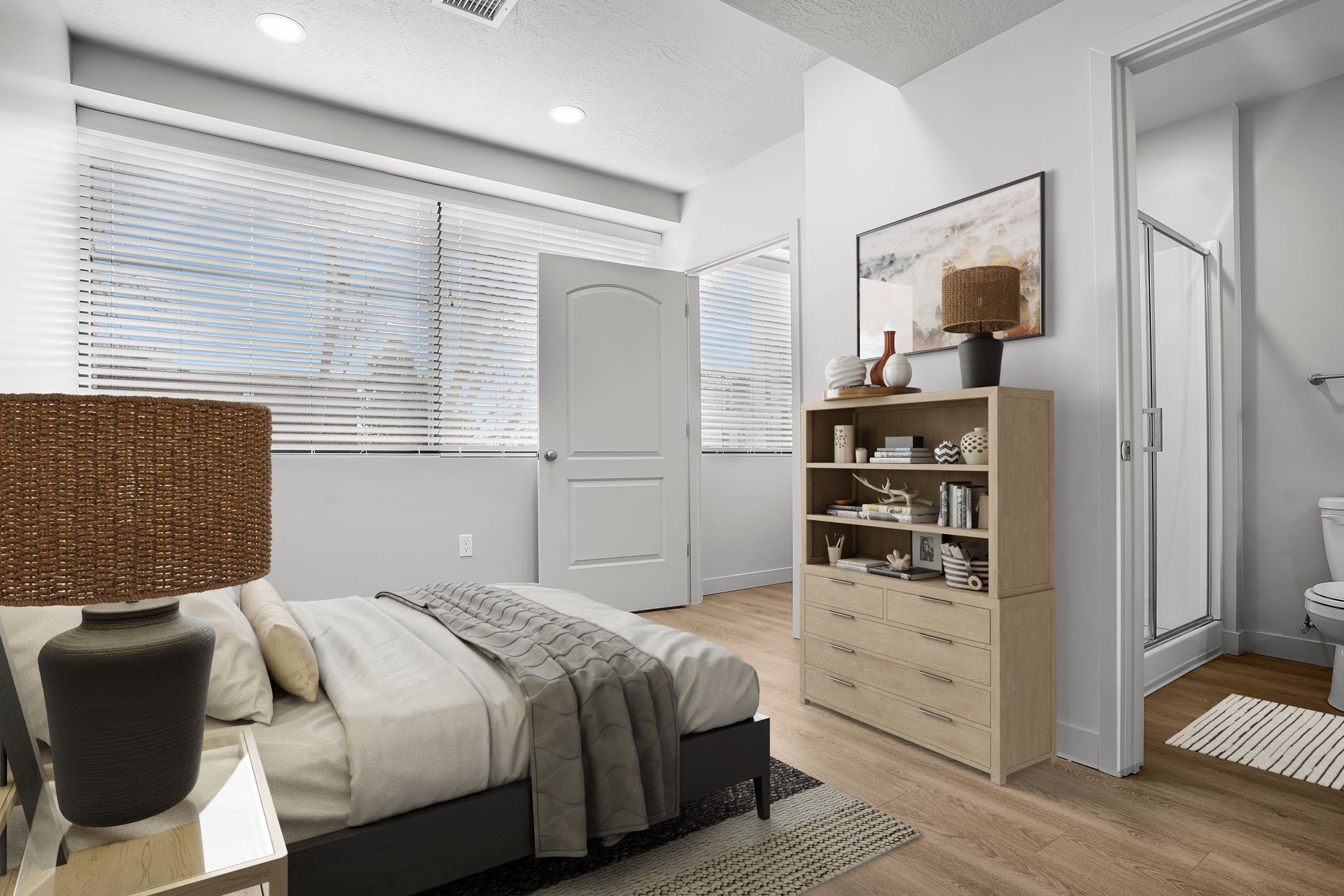 A bedroom with a bed , dresser , lamp and a bathroom.