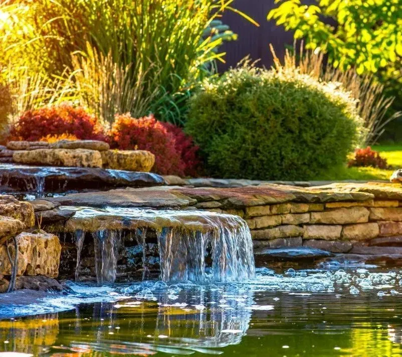 Decorative backyard waterfall with natural stone and shrubs.