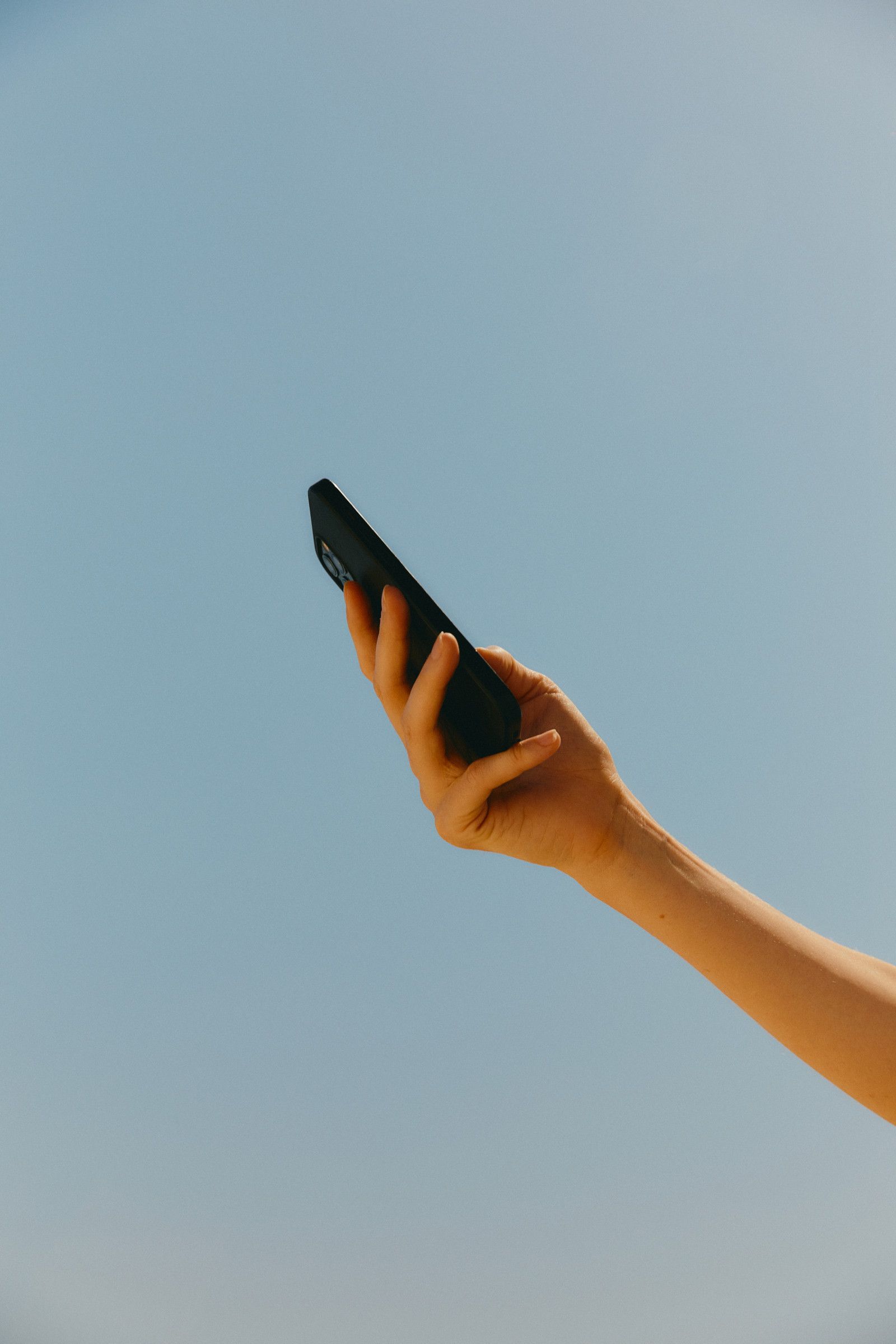 Hand holding a black smartphone against a clear blue sky