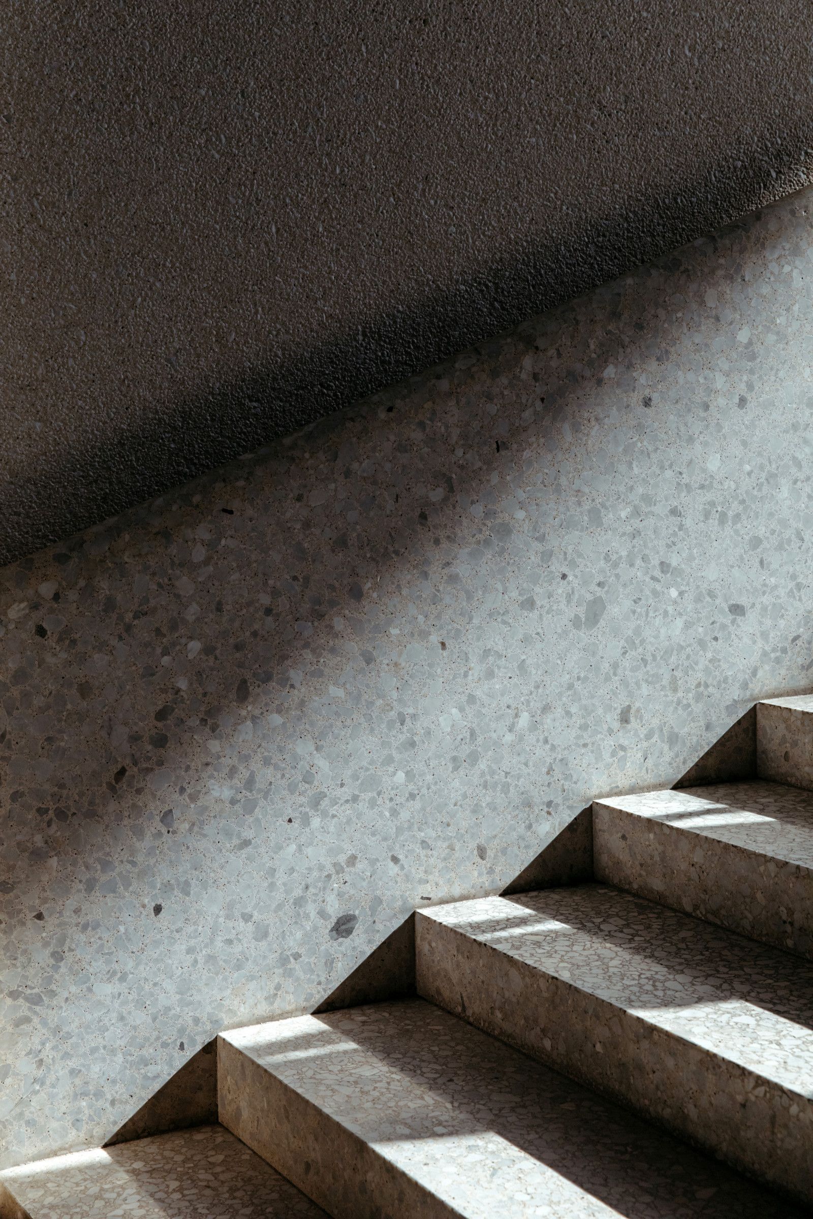 Staircase with dark steps beside a gray wall, lit by soft natural light.
