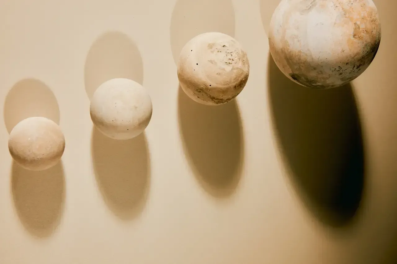 Four beige spheres casting long shadows on a tan background
