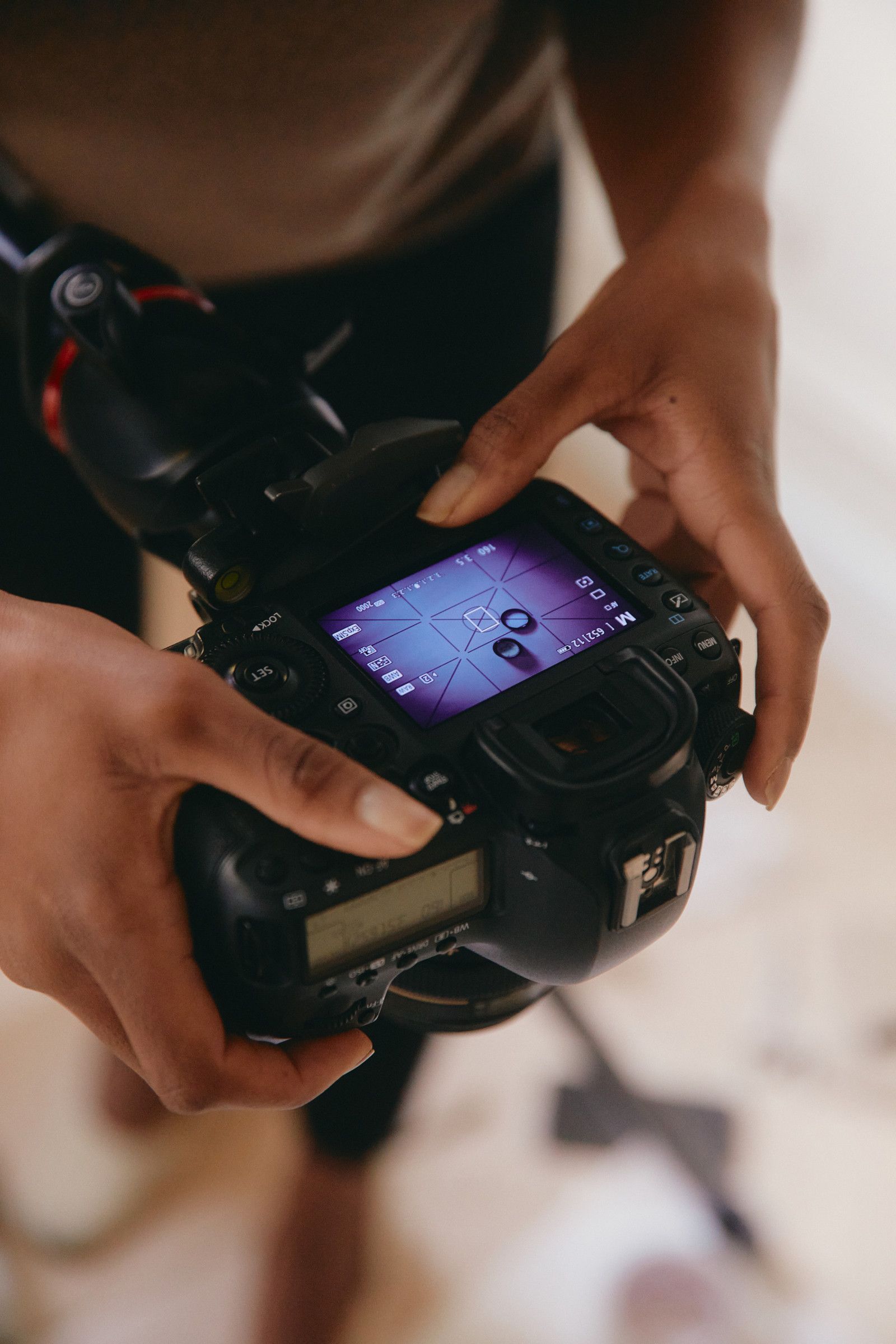 Hands holding a camera with its LCD screen glowing purple, viewed from above.