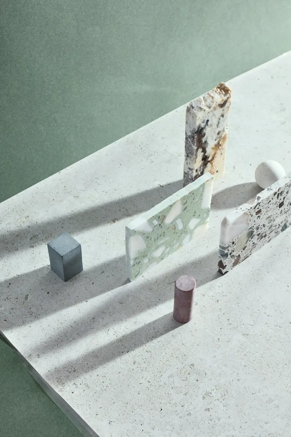 Minimalist tabletop scene with geometric shapes, shadows, and a weathered vertical post on a speckled white surface