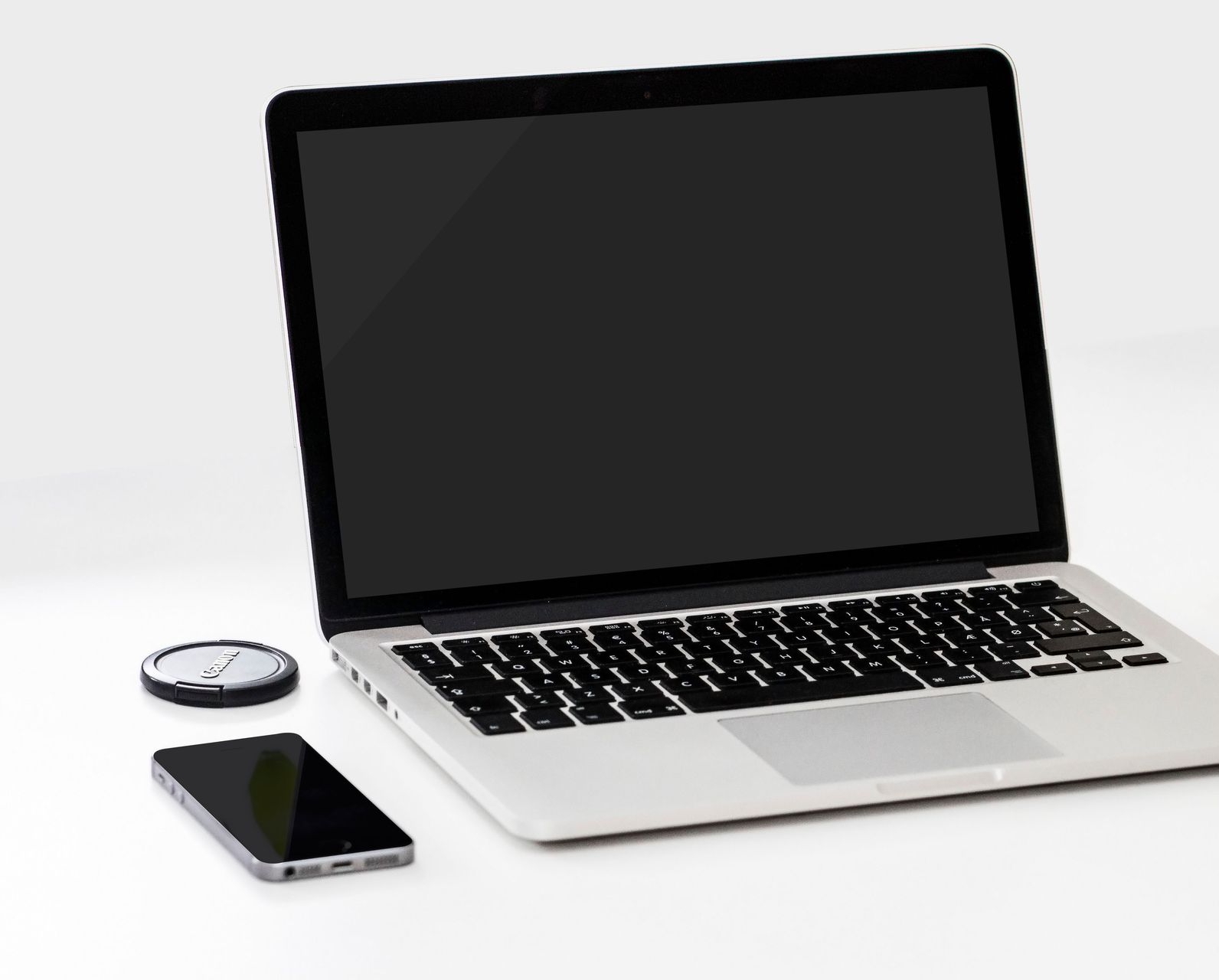 Silver laptop with black screen, smartphone, and wireless mouse on a white surface