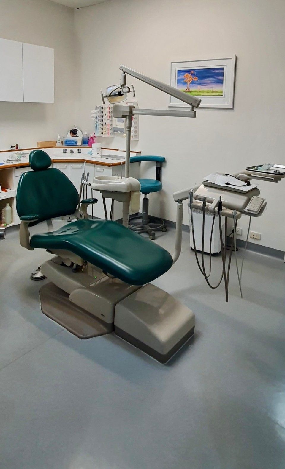 A dental office with a green dental chair and a sink.