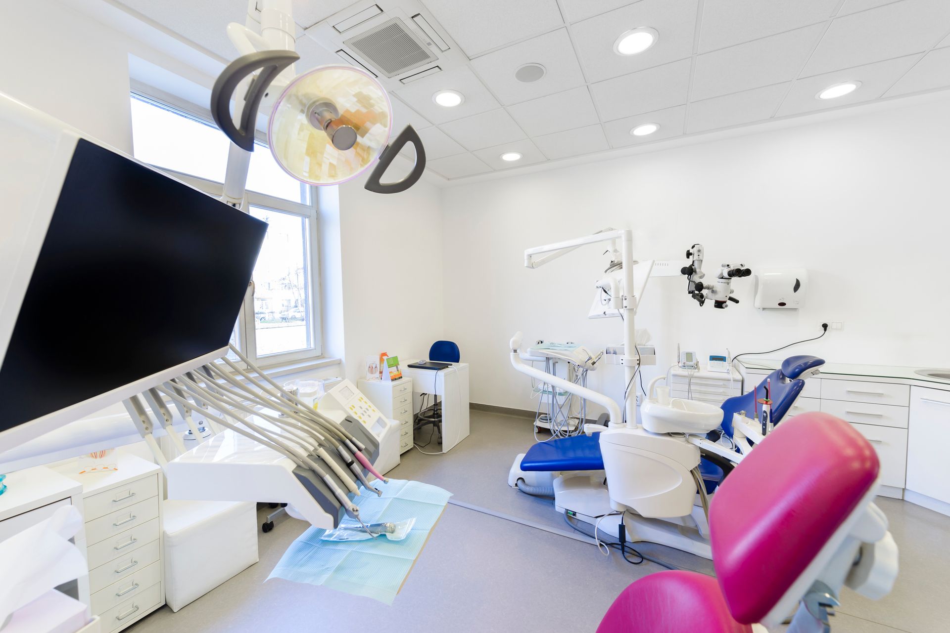 A dental office with a pink chair and a blue chair.