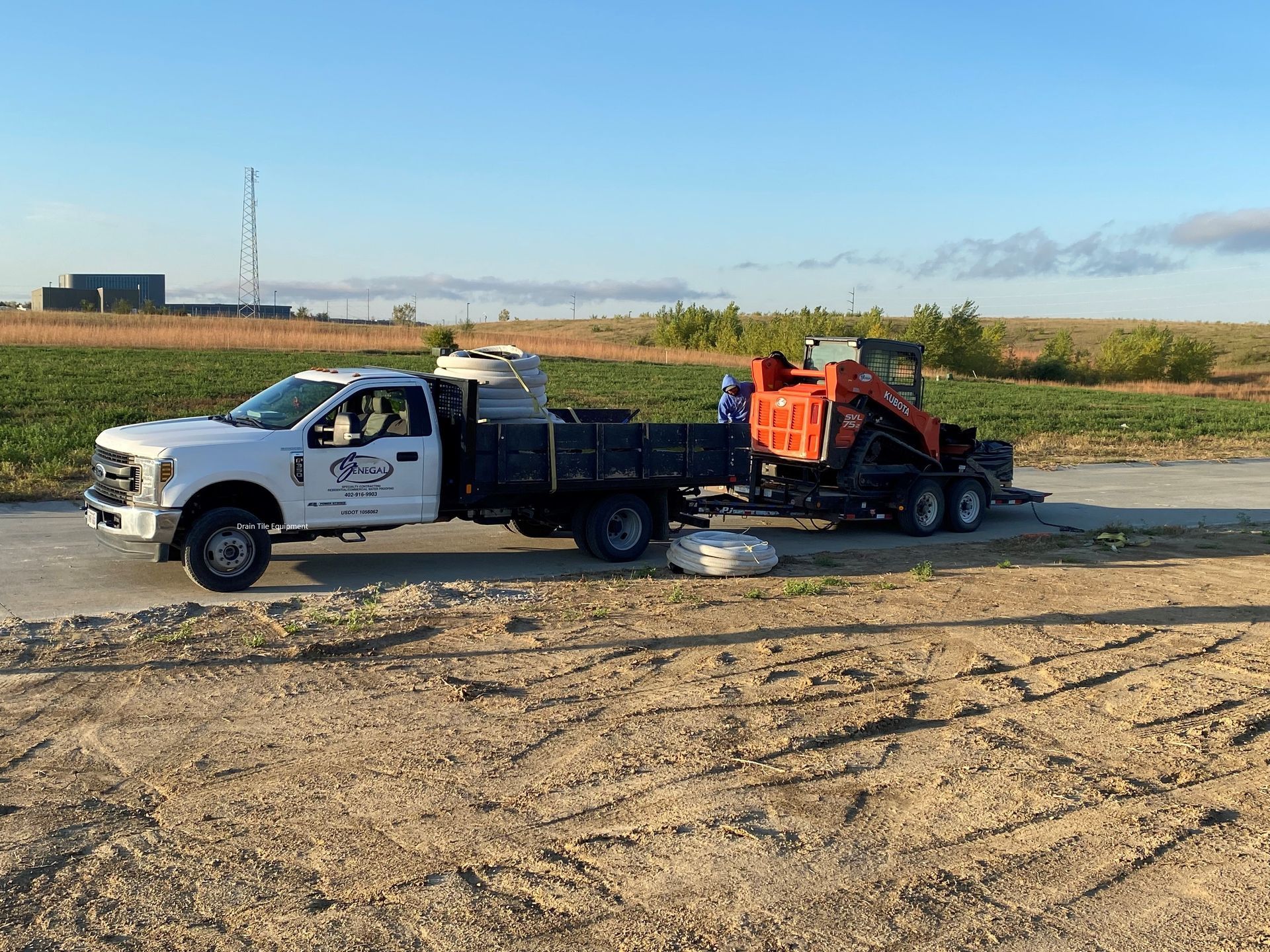 a white truck is towing a red tractor on a dirt road .