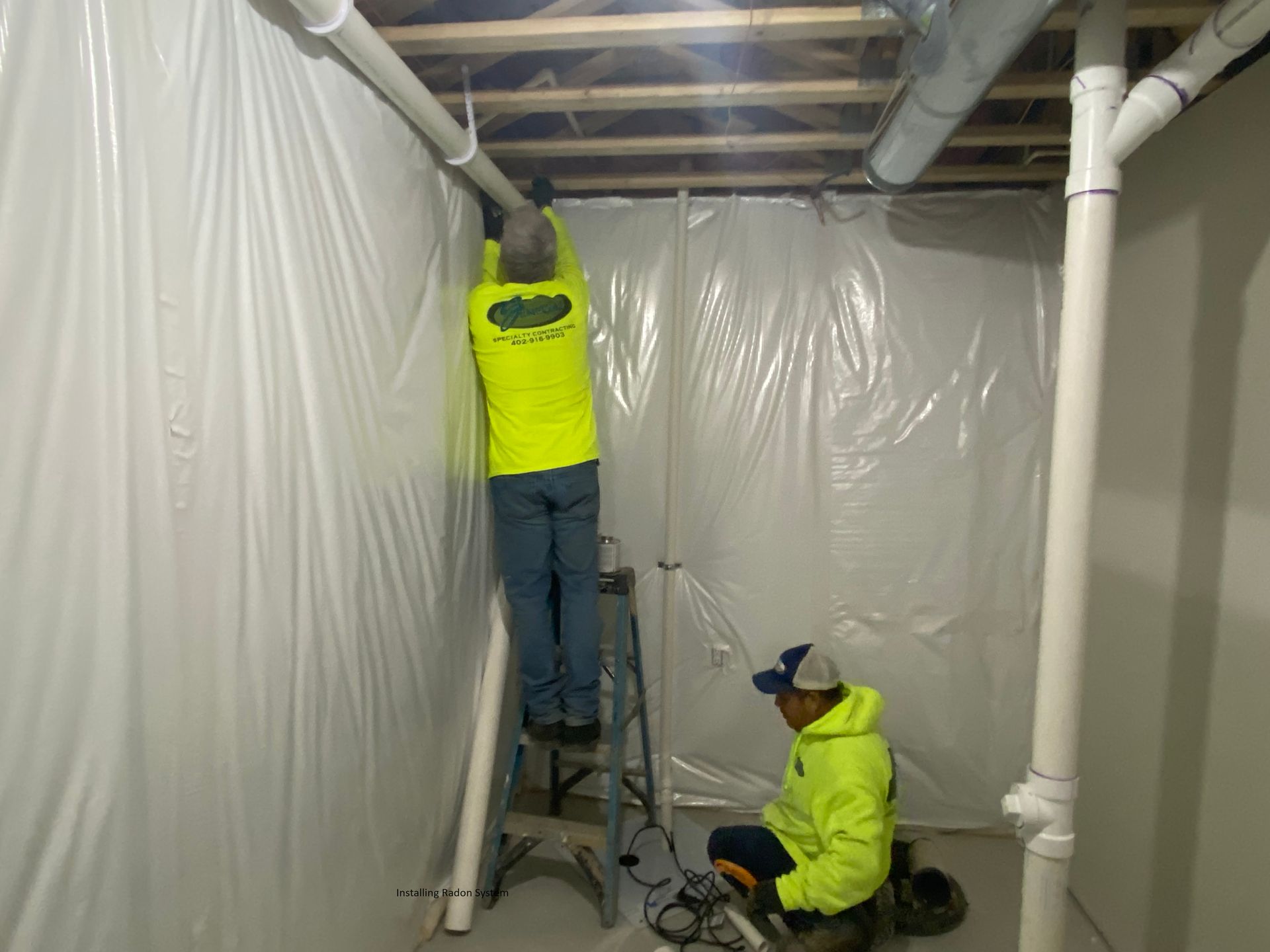 two men are working in a basement covered in plastic .