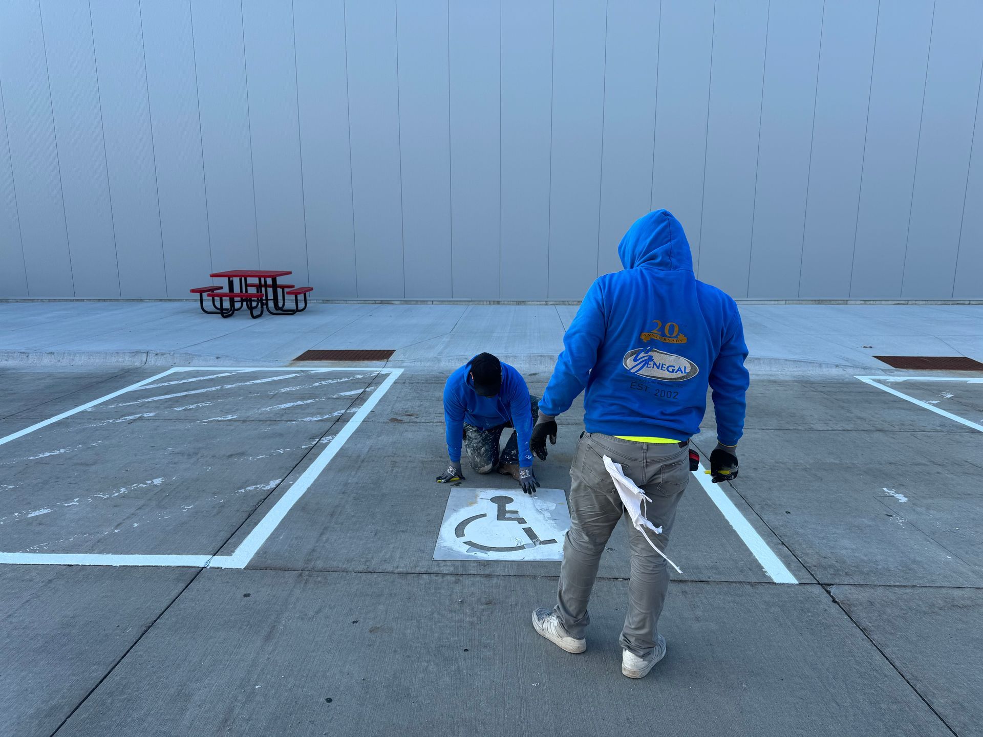 two men in blue hoodies are painting a handicapped parking space