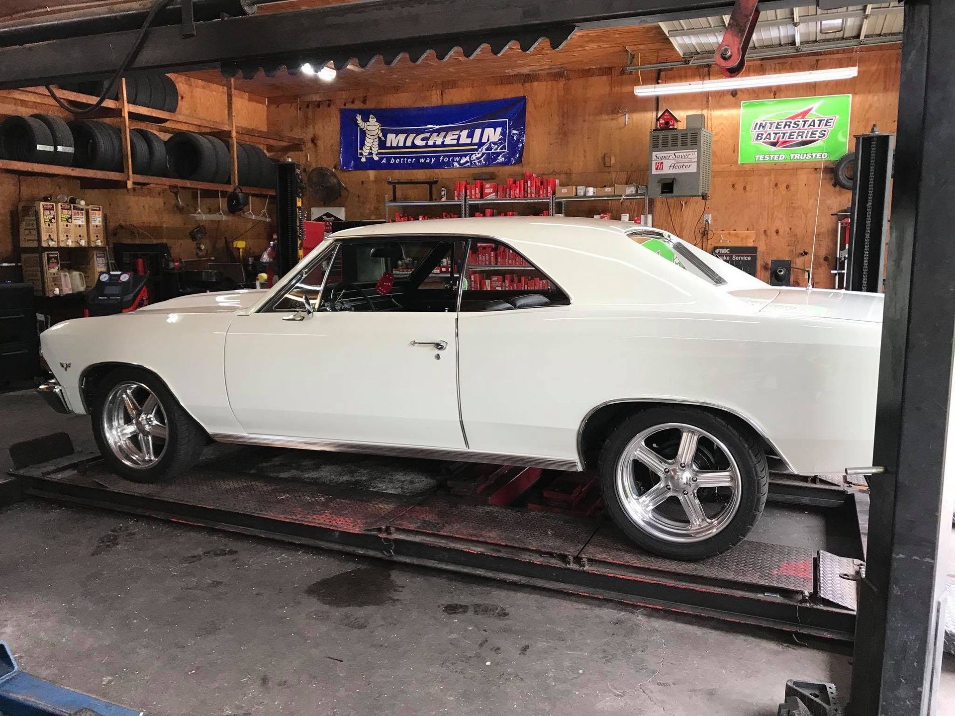 White classic muscle car in a garage on a lift, with tools and signs on the back wall | Lakeside Automotive