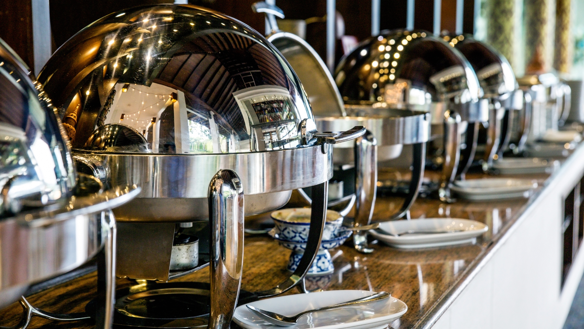 A buffet line with plates and silverware on a counter.