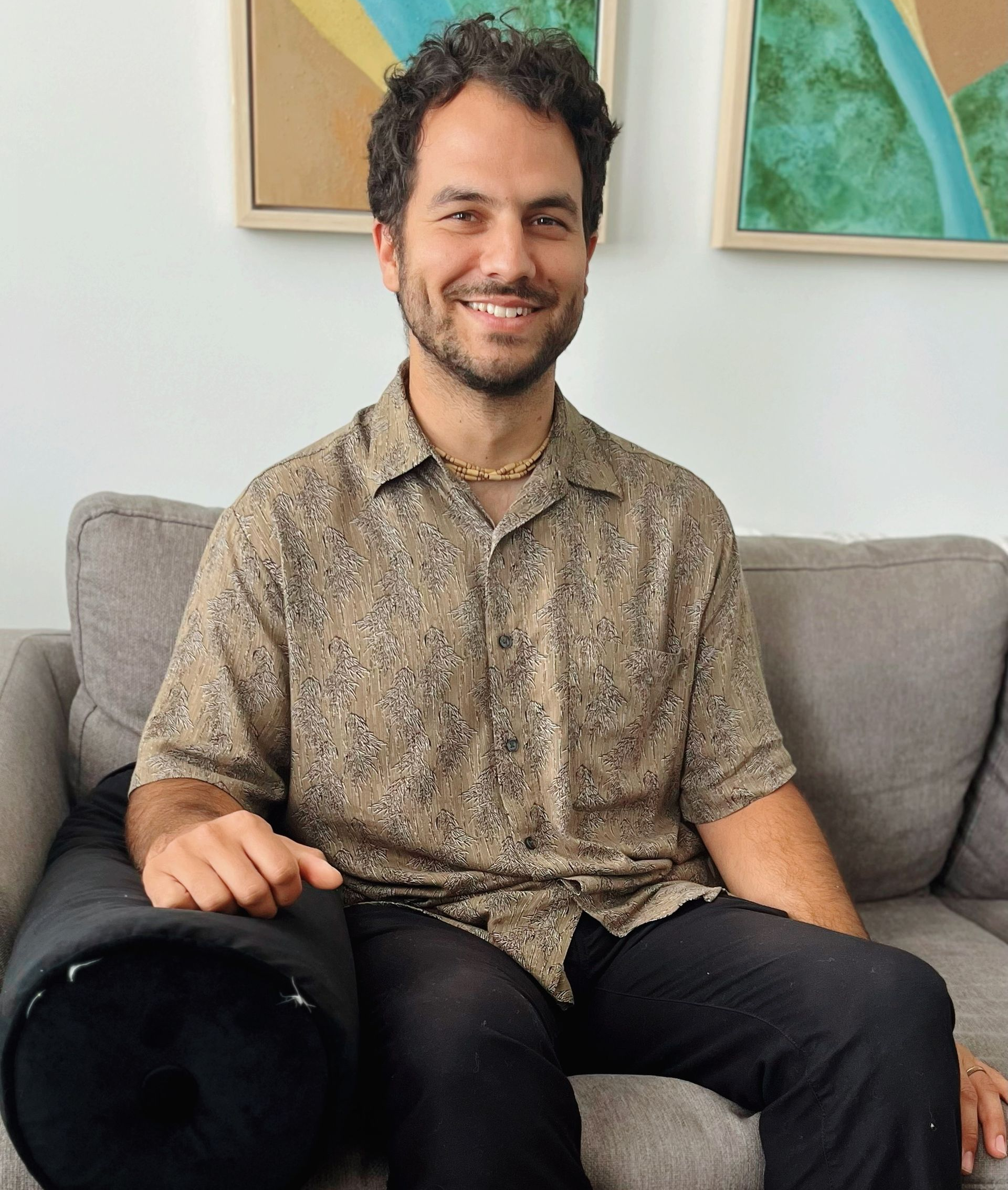 A man with a beard is comfortably sitting on a couch and smiling.