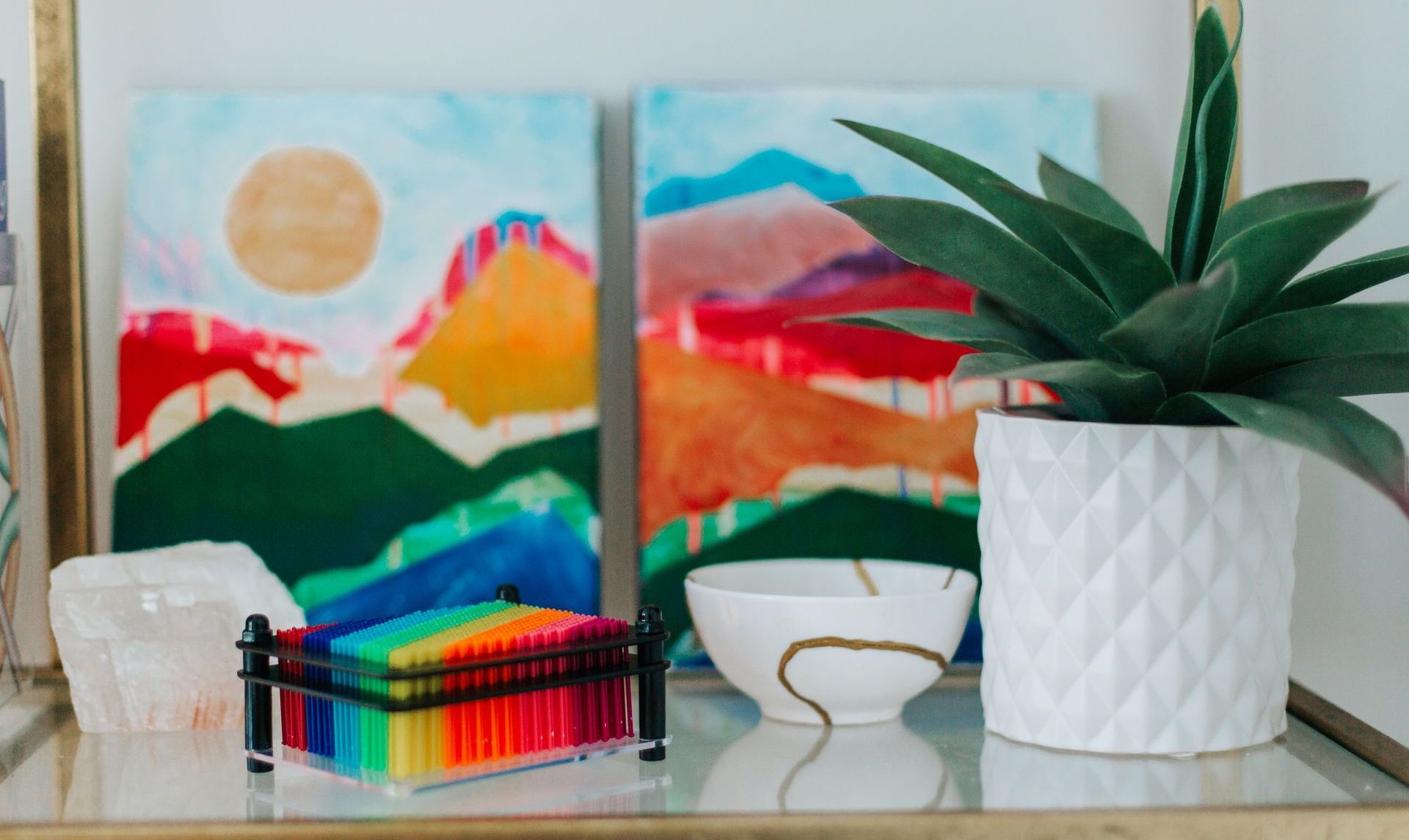 A shelf with a plant , bowls , and paintings on it.