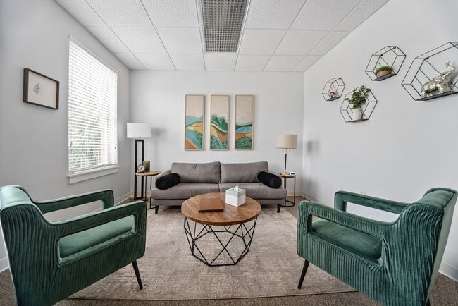 A living room with a couch , two chairs , a coffee table , and three paintings on the wall.