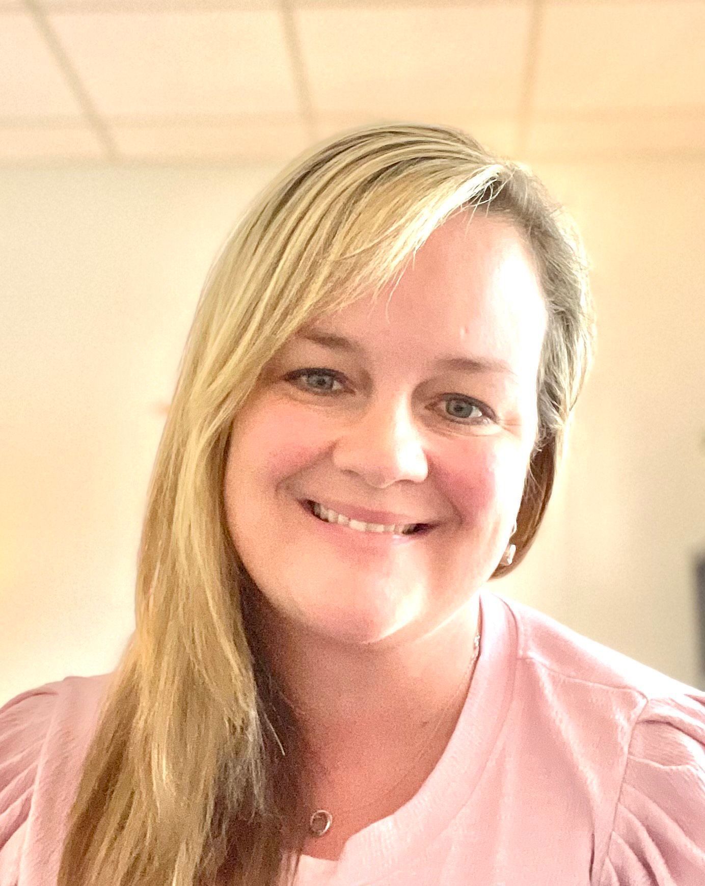 A woman in a pink shirt is smiling for the camera.