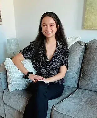 A woman is sitting on a couch with her legs crossed and smiling.