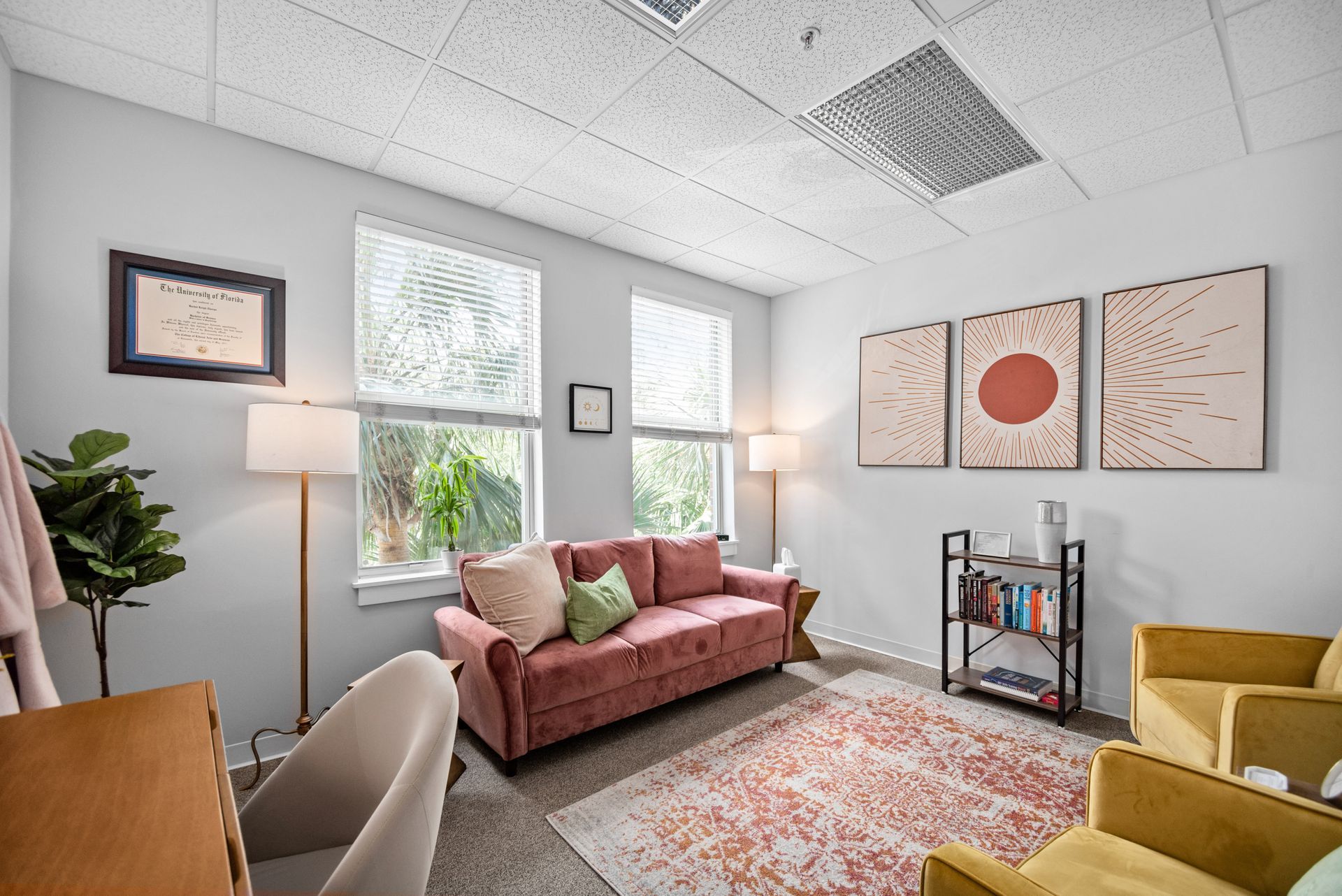 A living room with a pink couch , two chairs , a desk and a lamp.