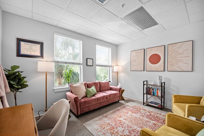 A living room with a pink couch , two chairs , a desk and a lamp.
