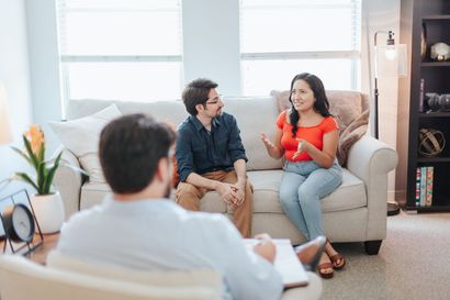 A man and a woman are sitting on a couch talking to a counselor.